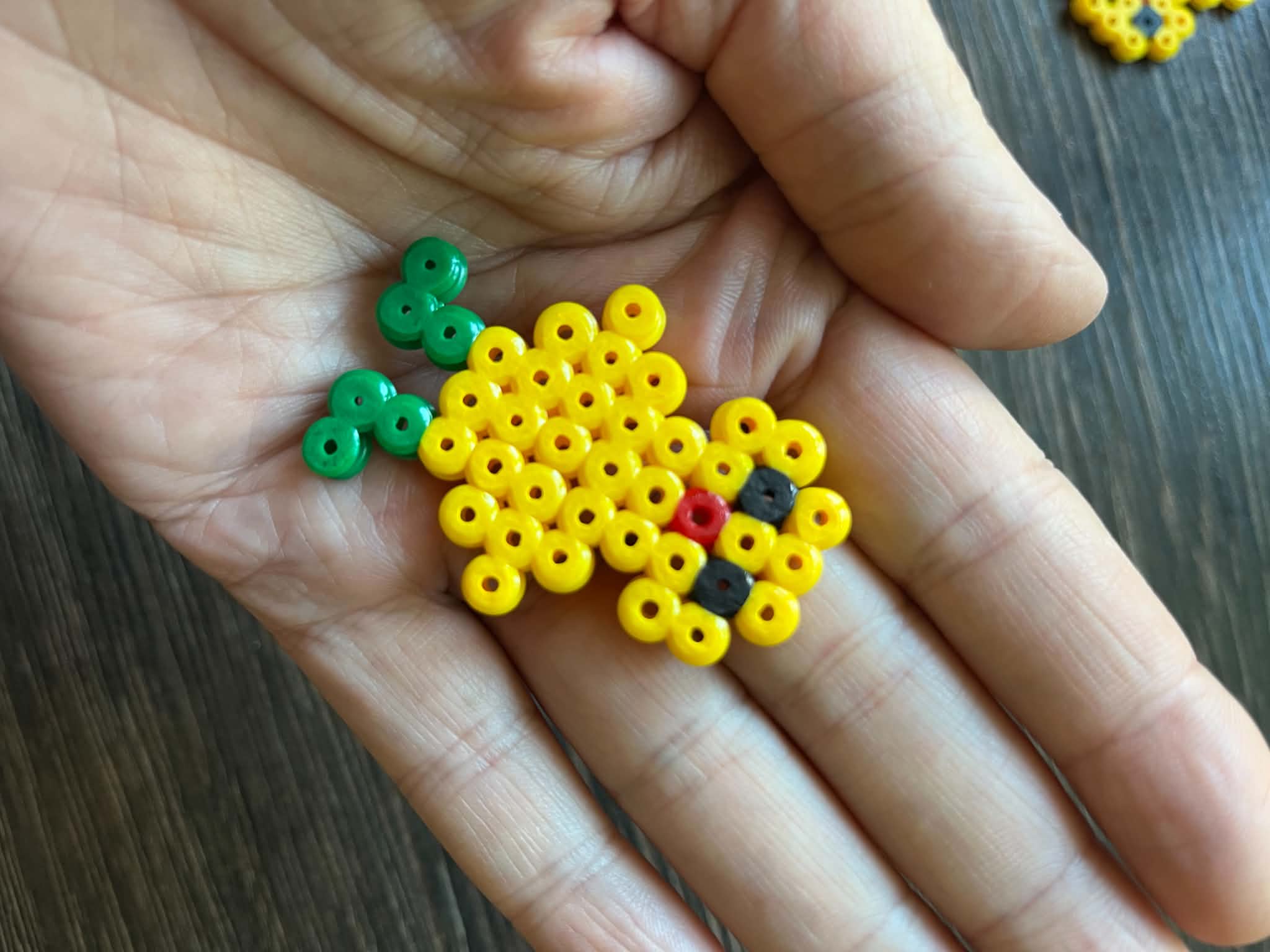 Håndlavet perlekylling af gule perler med grønne ben, holdt i en håndflade